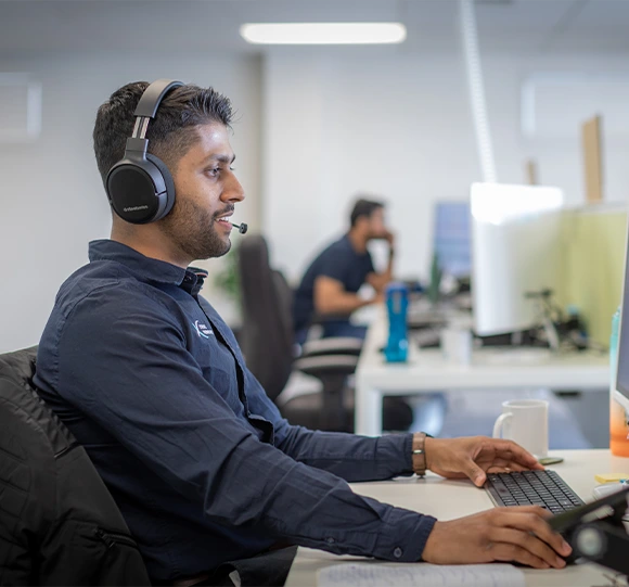 XP staff explaining solution to client on a video call. He's looking at the screen and wearing a headset. He is smiling and happy
