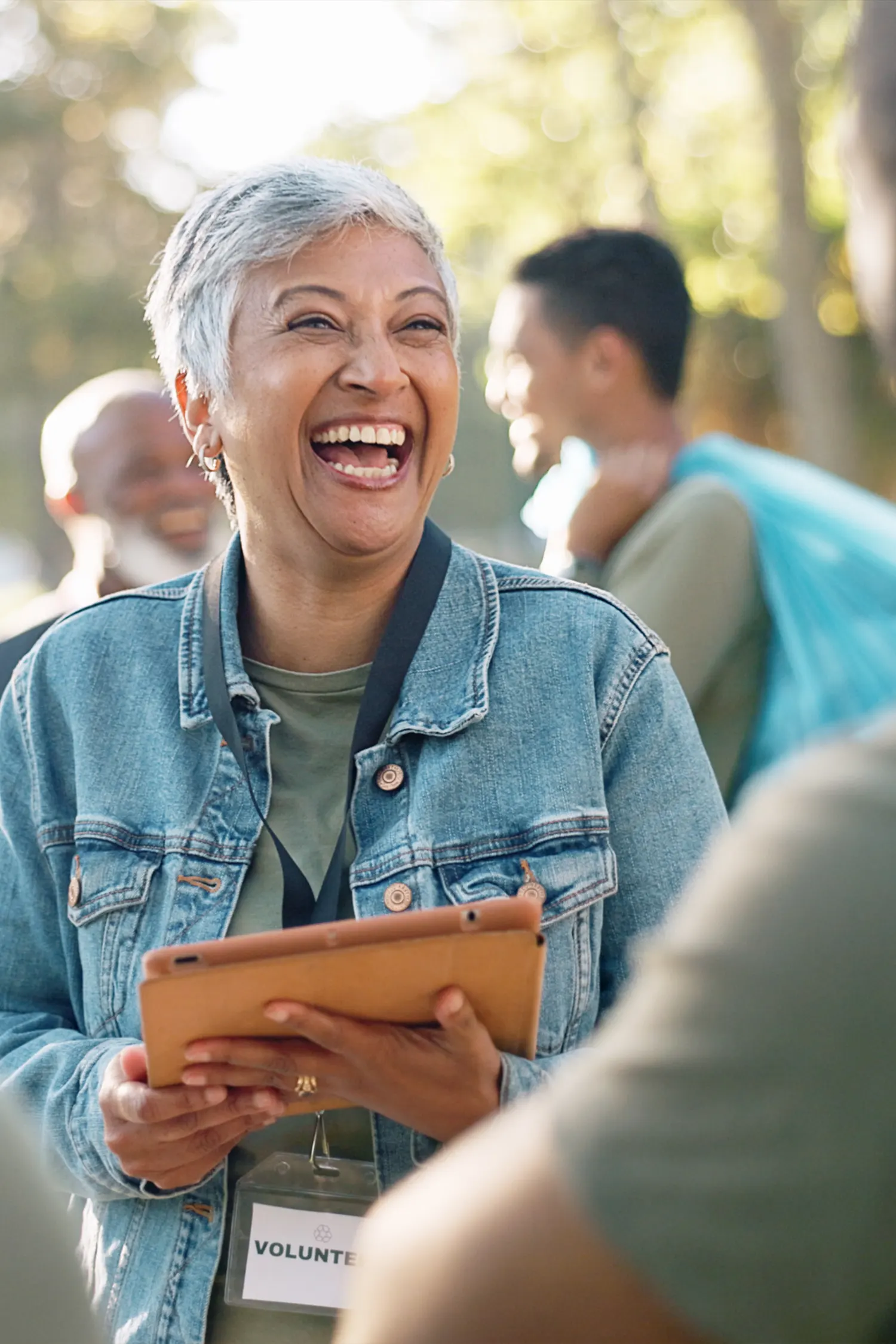 Woman laughing in a park holding an iPad. She's wearing a 