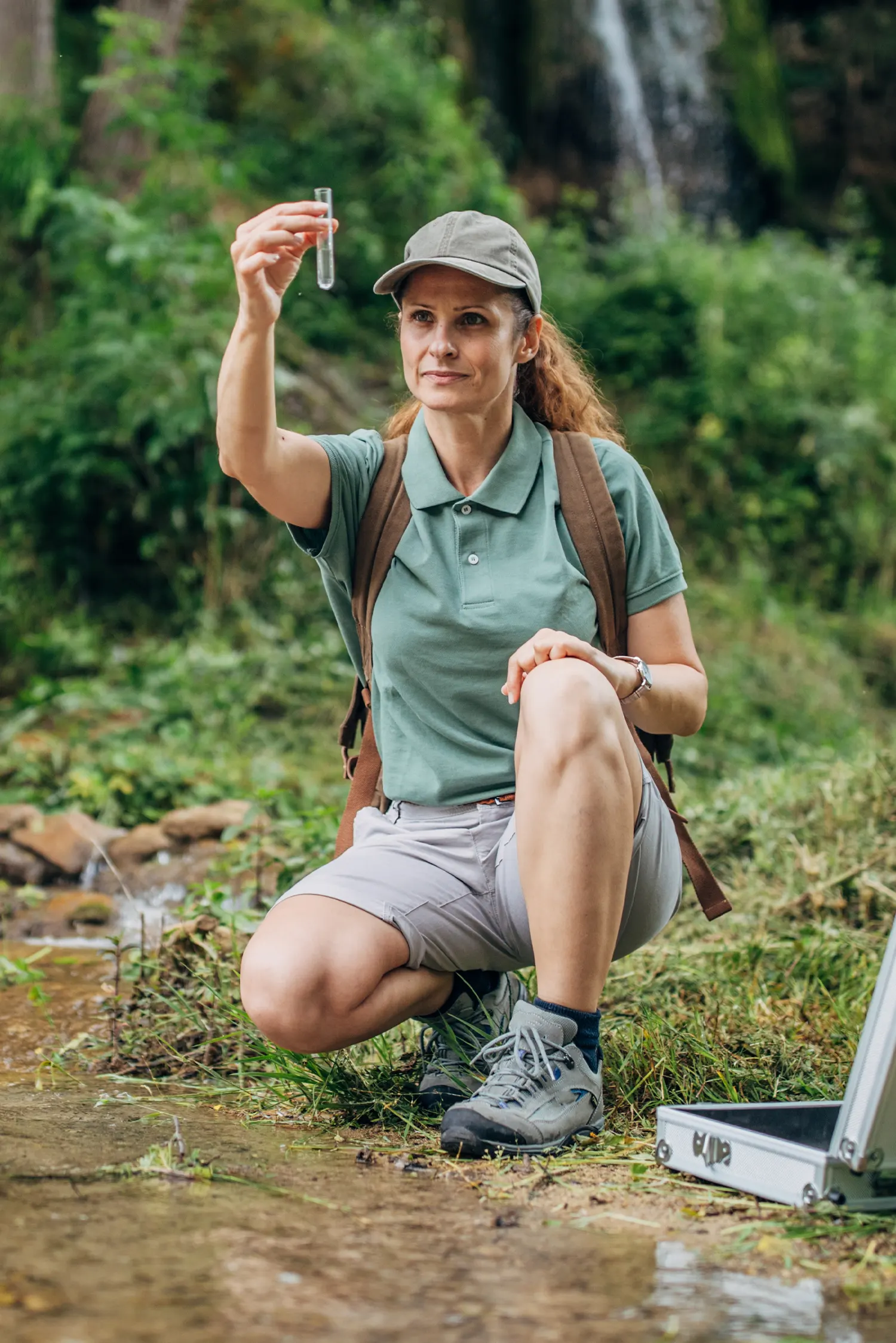 A woman crouched by a river in the wilderness checking water quality
