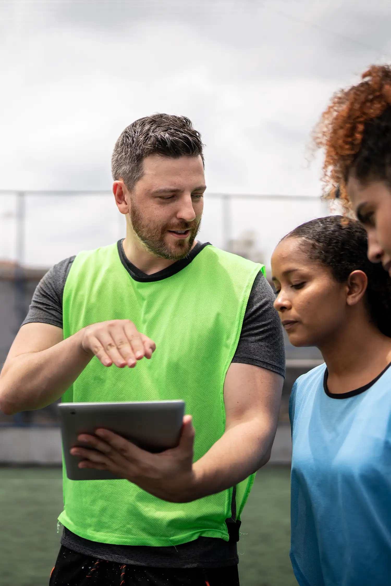 A coach standing with players, explaining and pointing to an ipad he's holding
