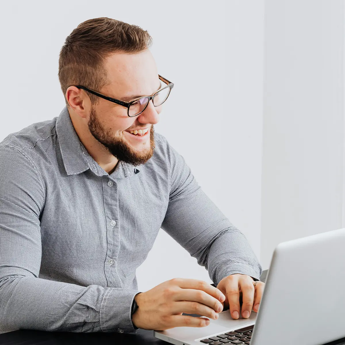 Man in a check shirt sitting with a laptop and smiling