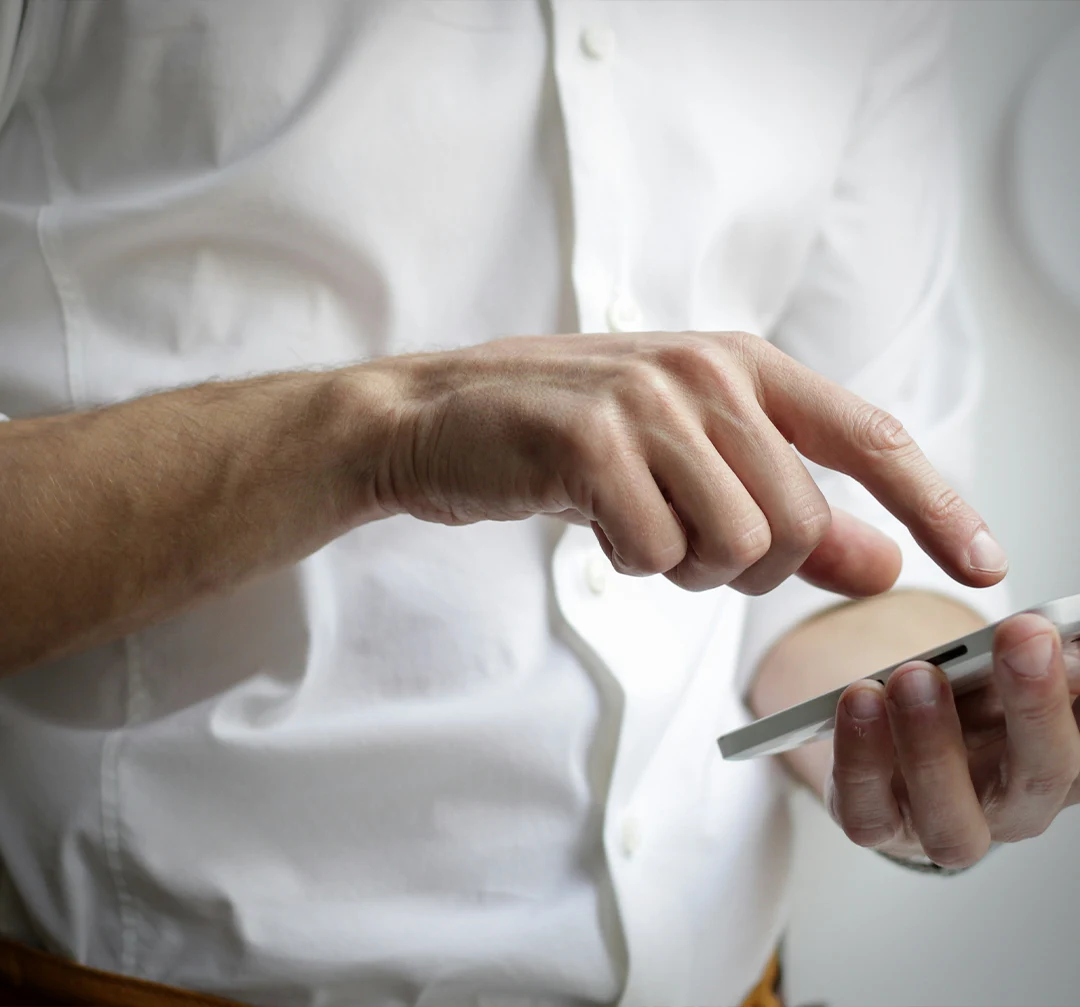 A man in a white business shirt holding a smartphone. His other hand is pointing at the screen about to touch it.