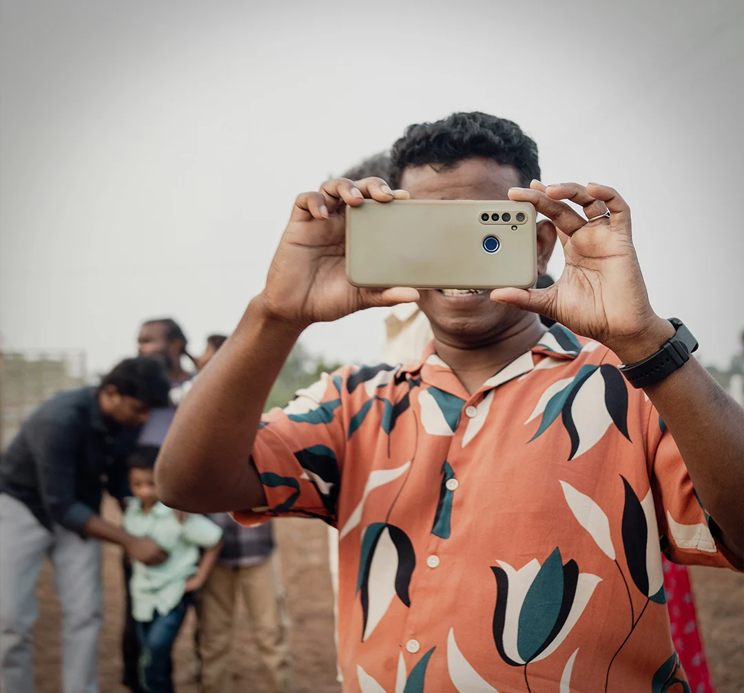 An asian man in a pink shirt holding up a smart phone and taking a picture