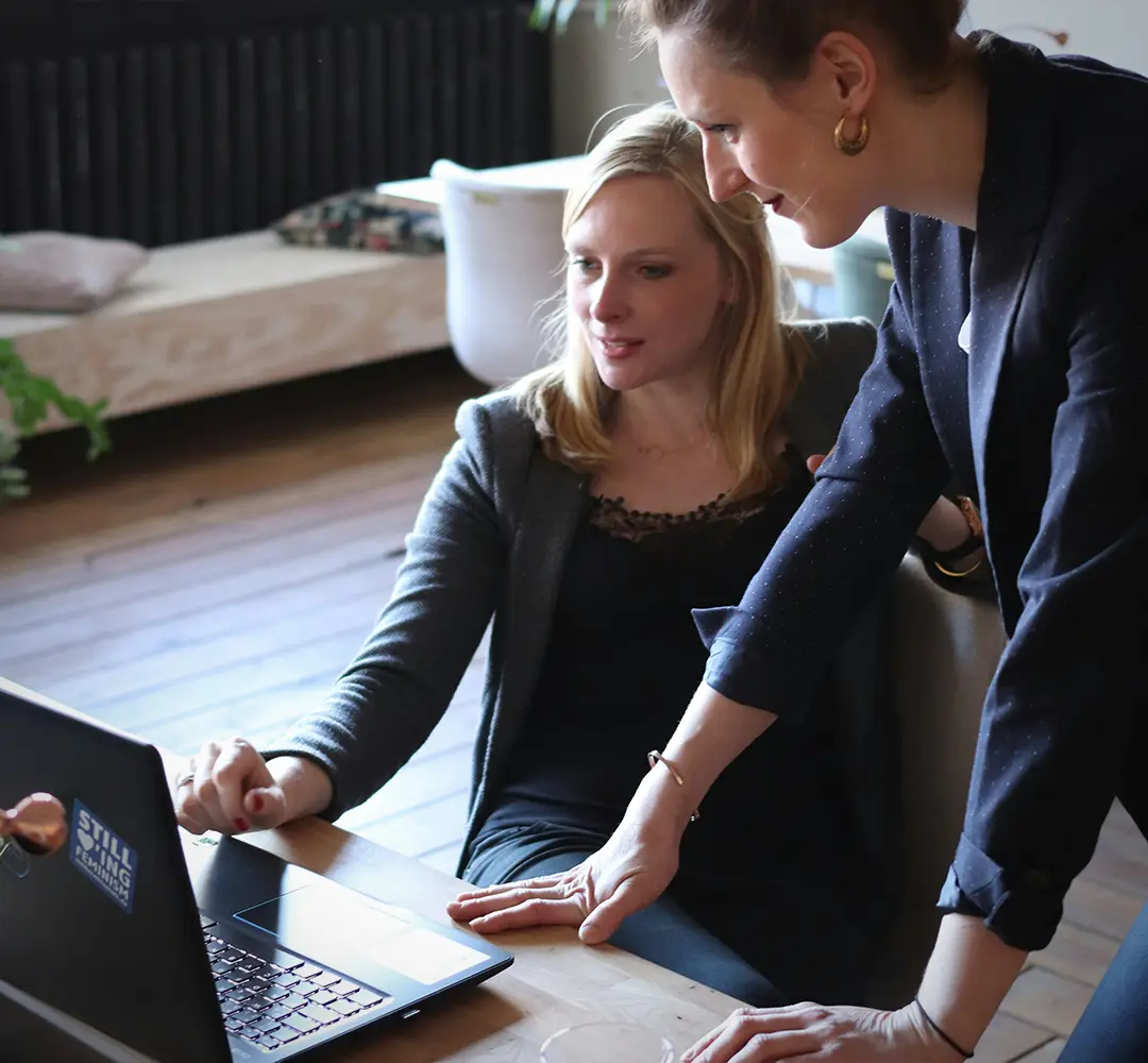 two women in business attire, looking at a laptop