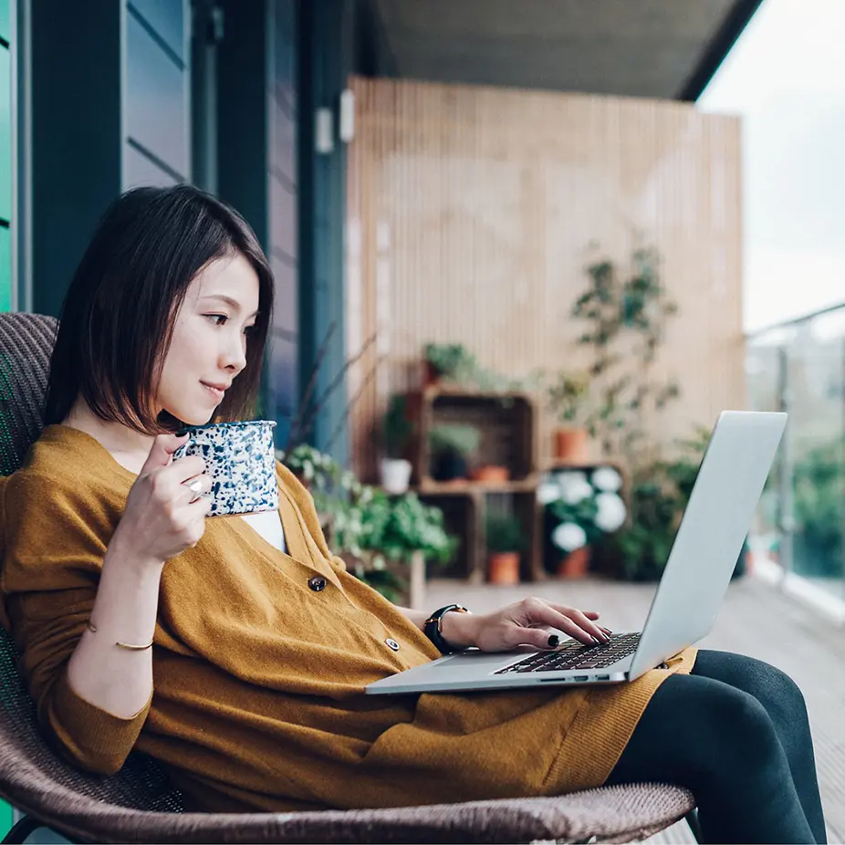 lady sitting drinking a coffee out of a mug, looking at her laptop in her lap