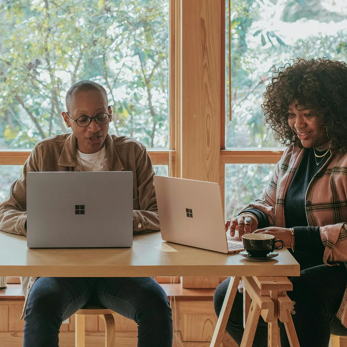 two people, a man and a woma, sitting at a desk looking at their microsoft surface laptops
