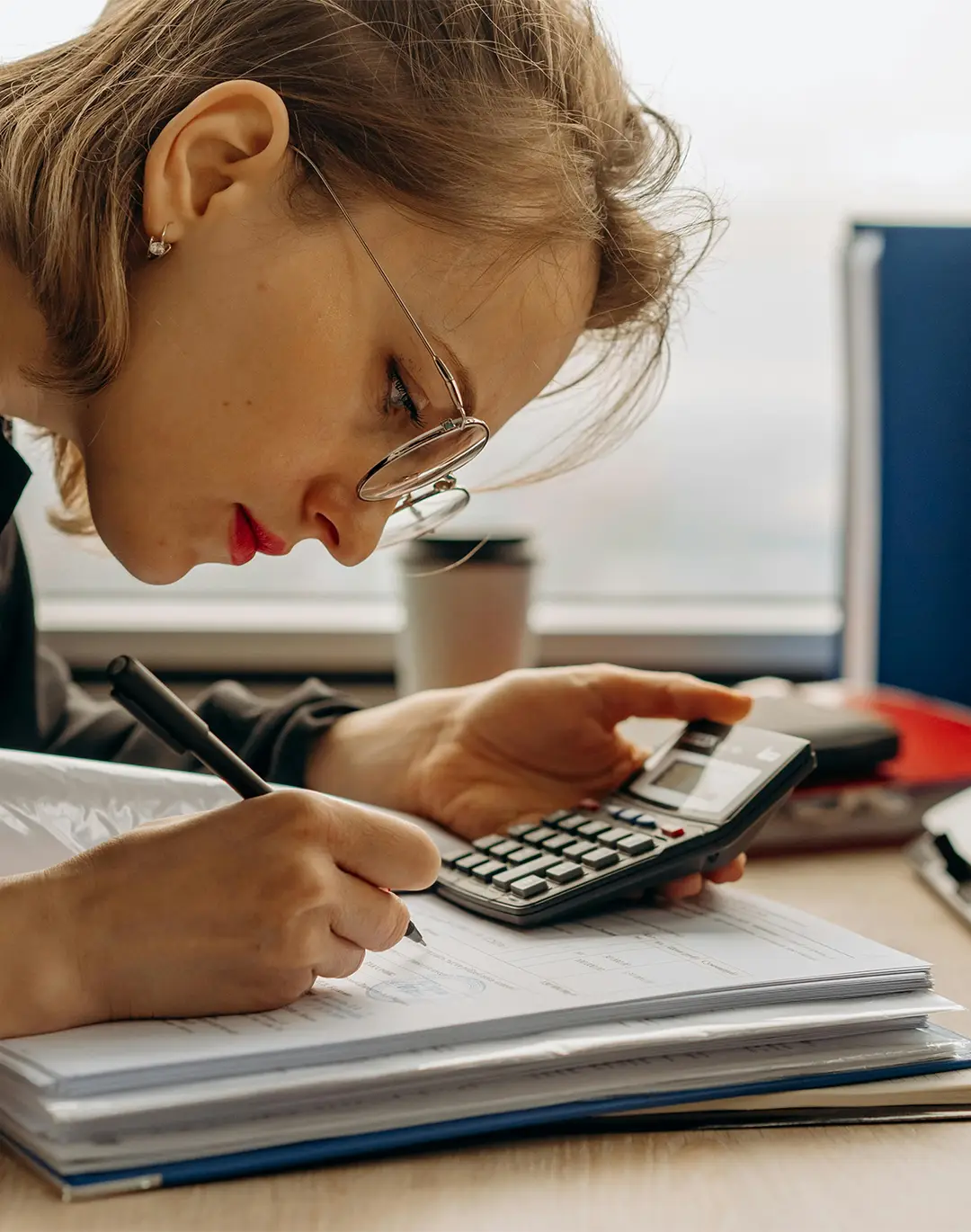 woman leaning over accounts holding a pen in one hand and a calculator in the other
