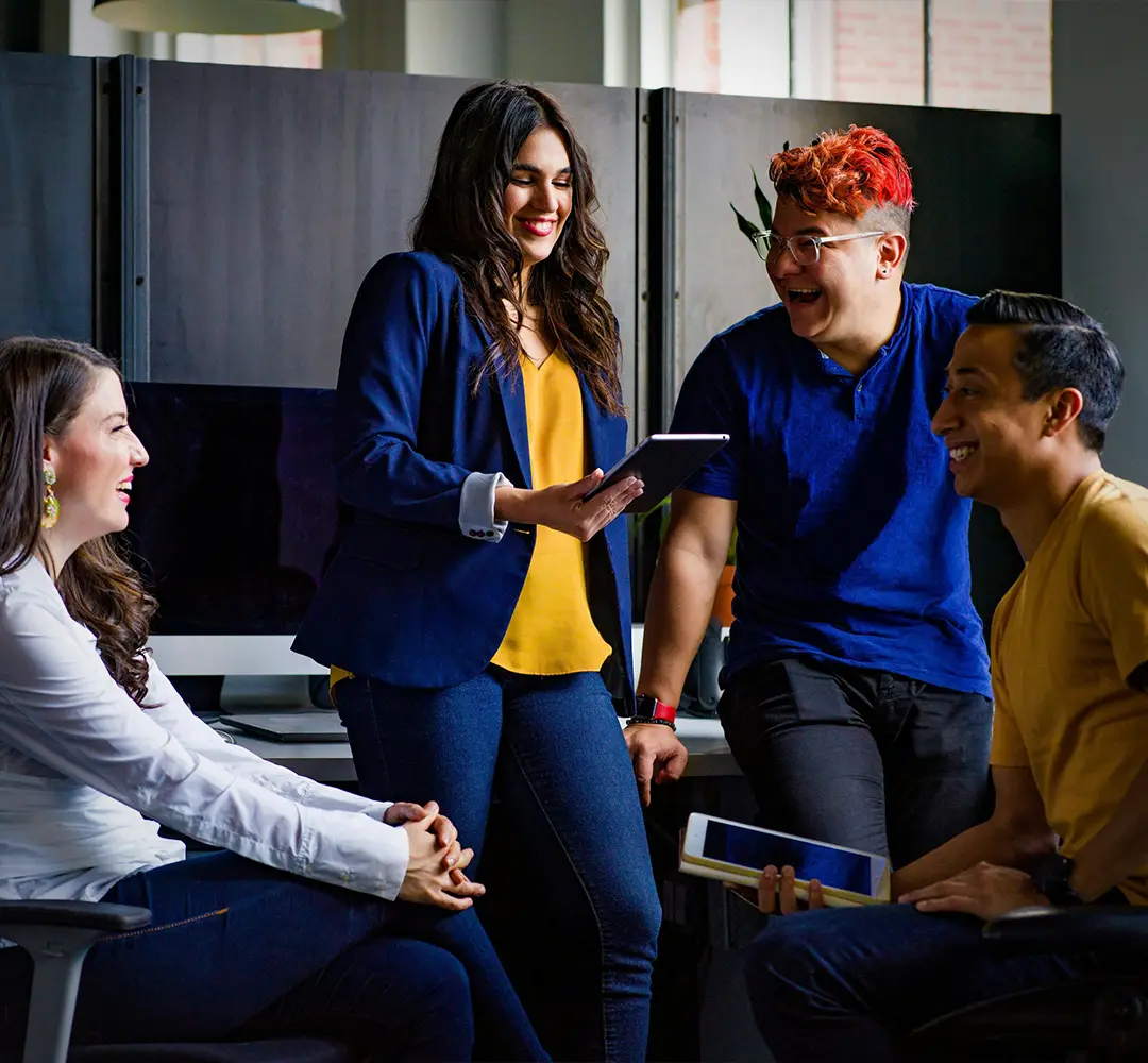 Two women and two men gathered together in a modern office, talking and laughing together