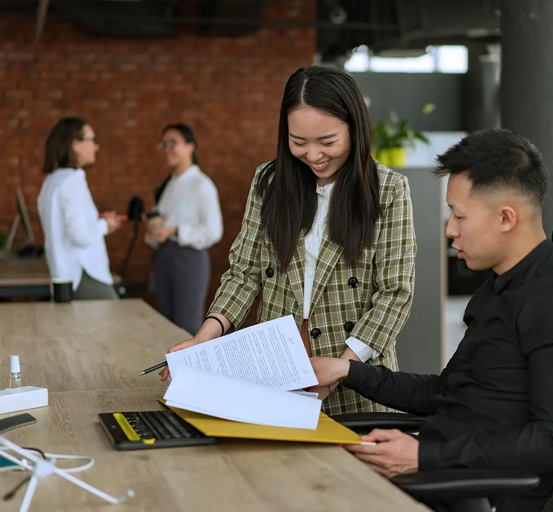 An asian woman sharing documents with an asian man sitting at a desk